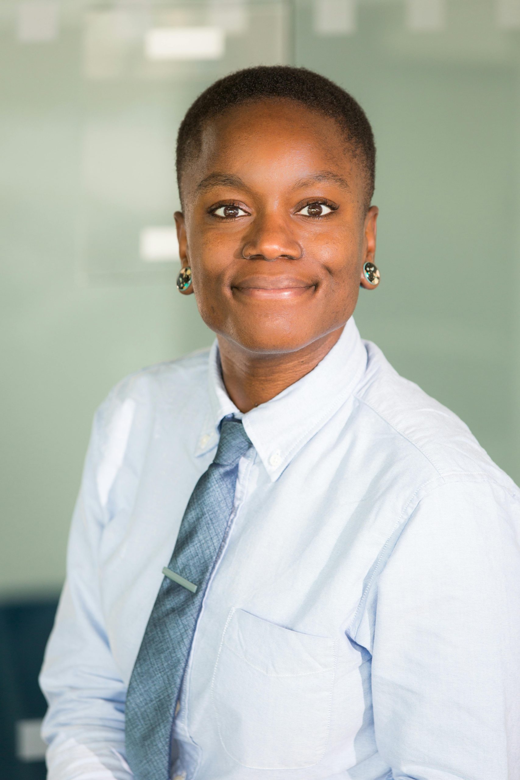 Smiling woman in office setting, wearing formal attire, exuding confidence.